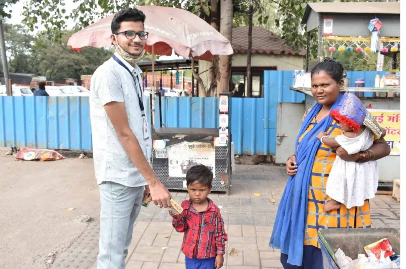 A ReadoBook volunteer on a Pune street handing something to a small child while the child's mother looks on.